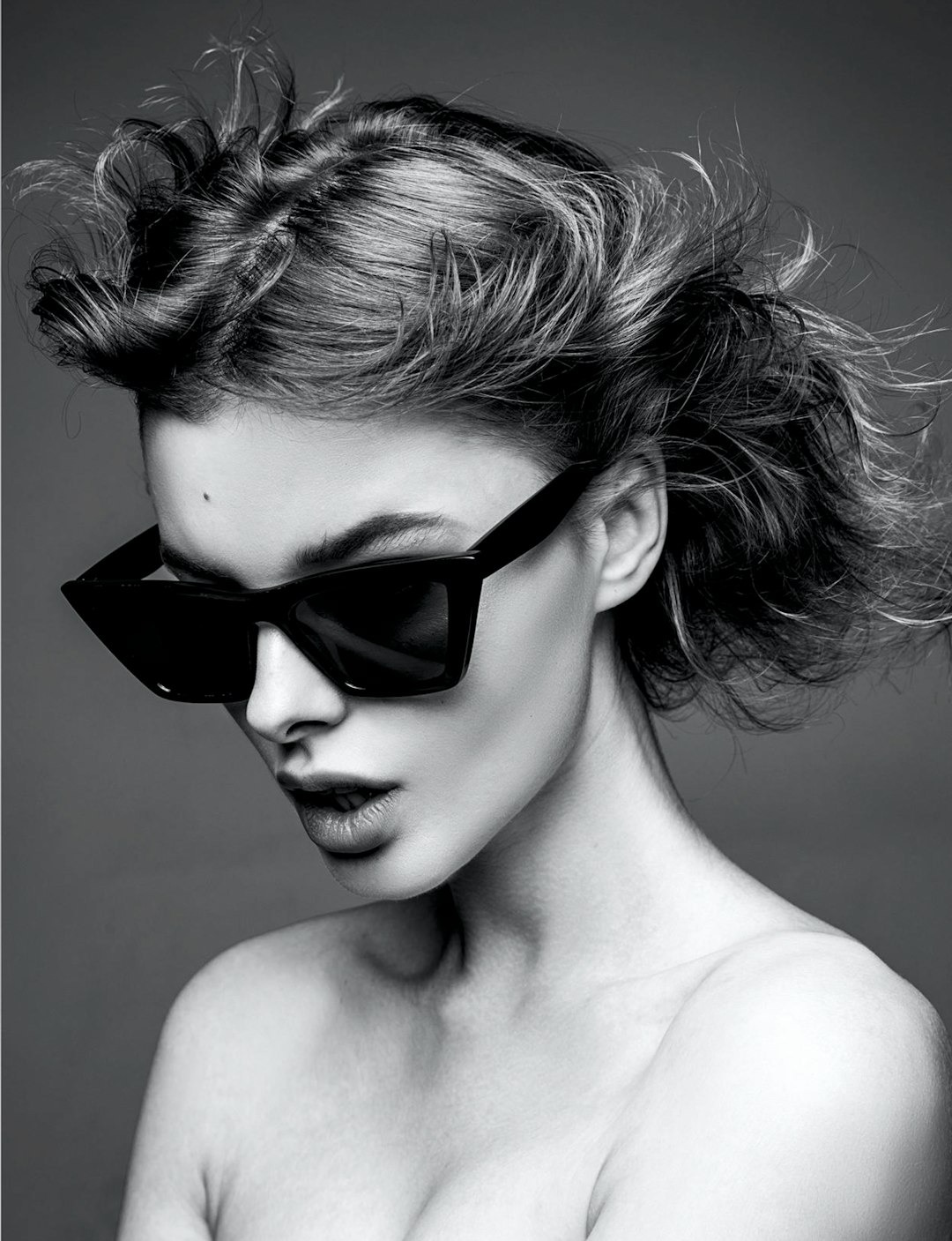 Woman with a voluminous updo wears angular black sunglasses.